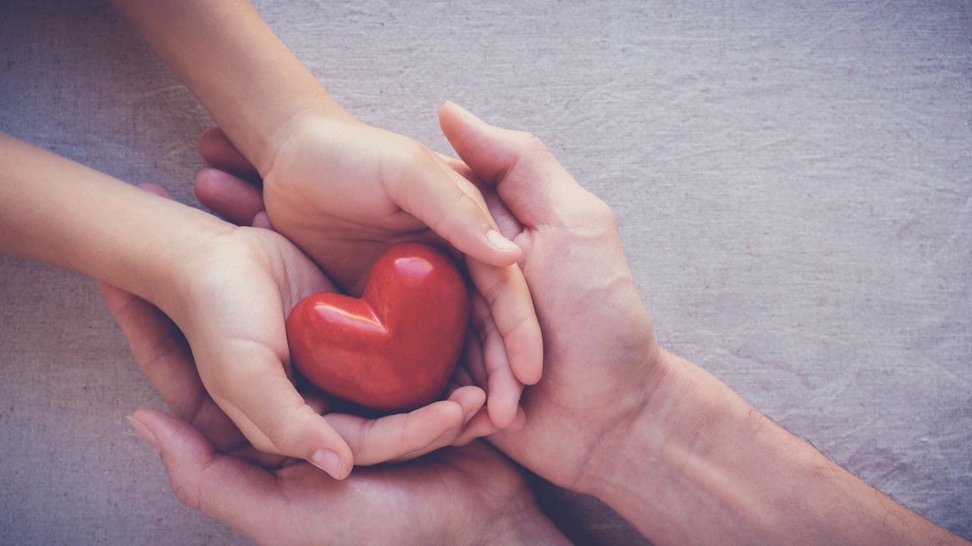 Adult and child hands holding a red paper heart.
